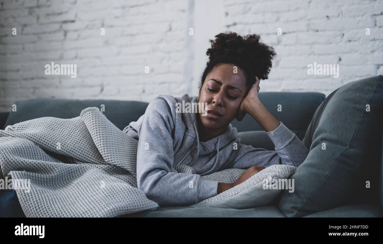Young attractive african american woman lying at home living room couch feeling sad tired and worried suffering depression, distress and anxiety in me Stock Photo