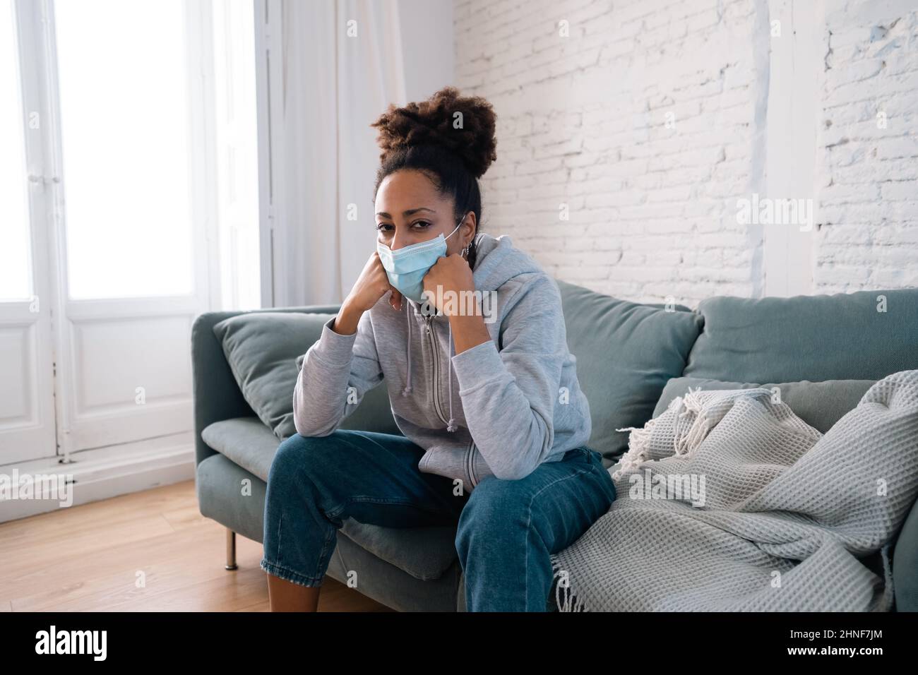 Young afro latina young woman with protective face mask on sofa feeling ill, exhausted and sad. Depressed african american teen tired of stress, tensi Stock Photo