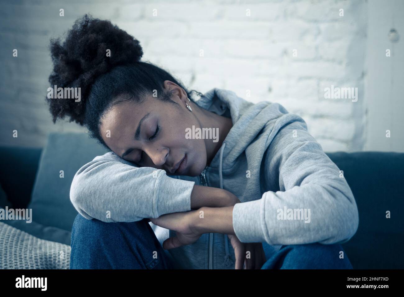 Lonely young afro latina young woman on sofa feeling in pain, exhaustion and sadness. Depressed hispanic or afro american girl at home, looking away w Stock Photo