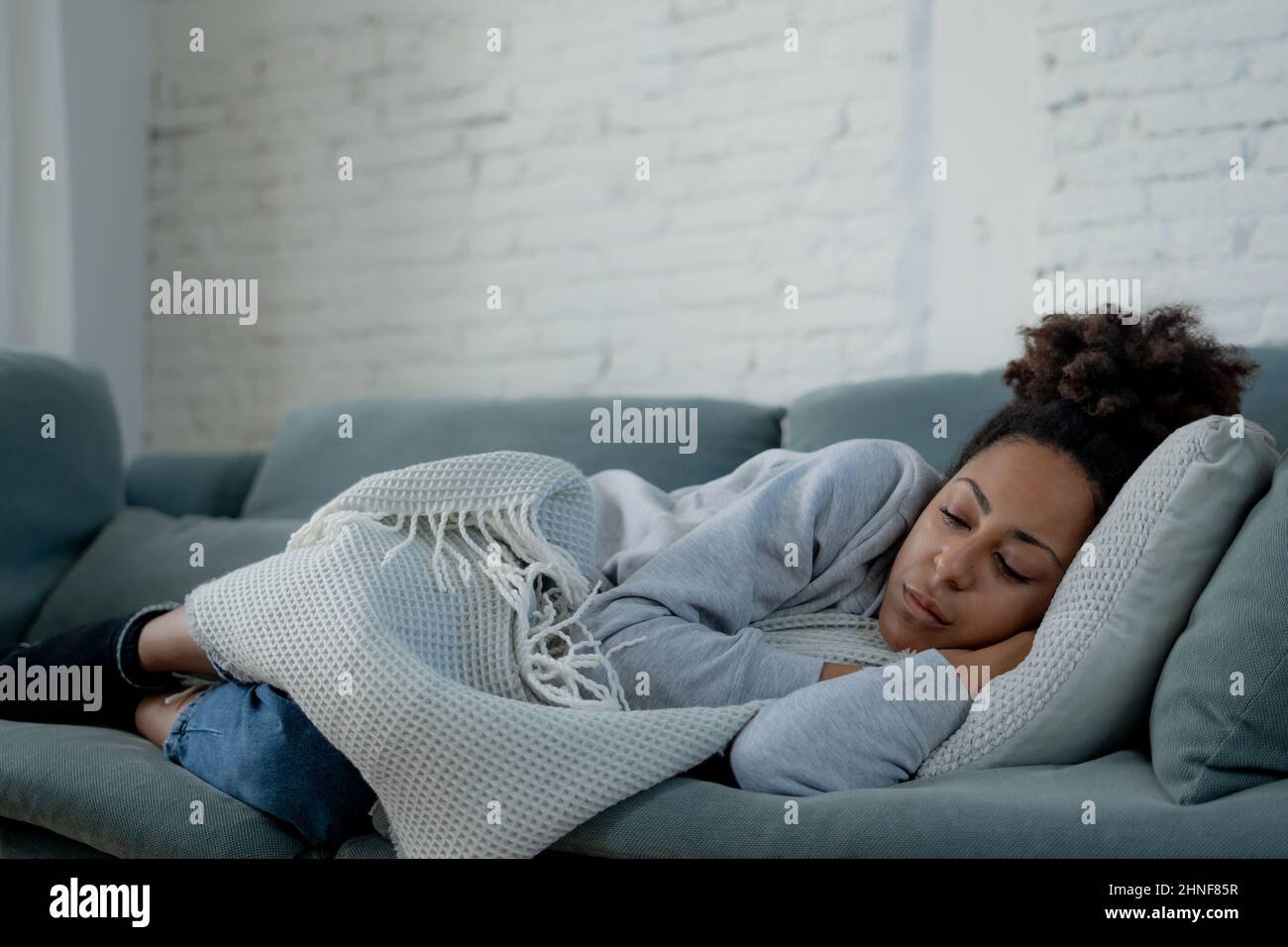Lonely young afro latina young woman on sofa feeling in pain, exhaustion and sadness. Depressed hispanic or afro american girl at home, looking away w Stock Photo
