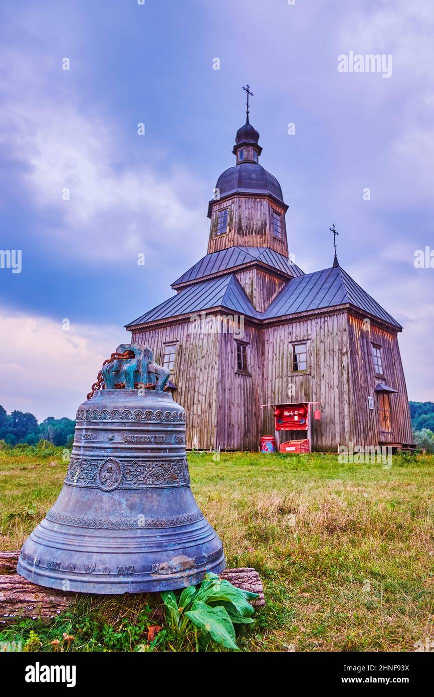 The bronze bell and historical wooden St Nicholas Church in Cossack Village Scansen, Ukraine Stock Photo