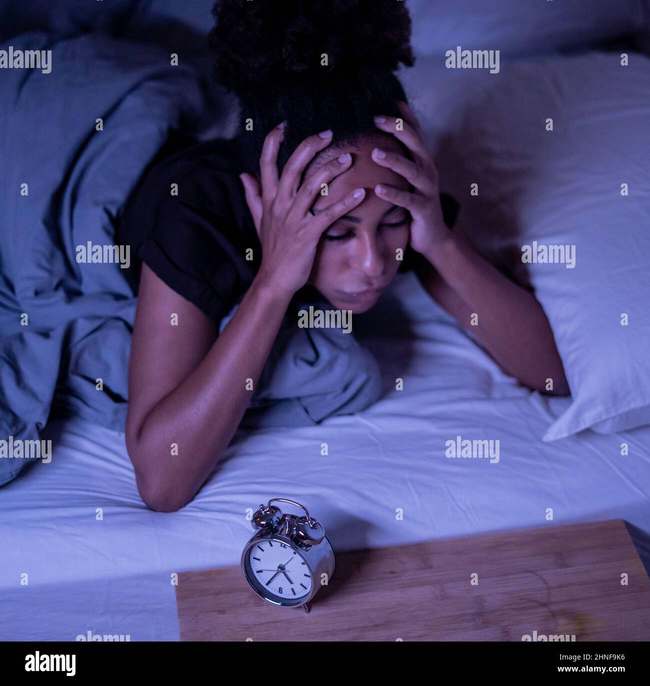 Sleepless and desperate beautiful afro american woman awake at night not able to sleep looking at clock suffering from insomnia in sleep disorder and Stock Photo