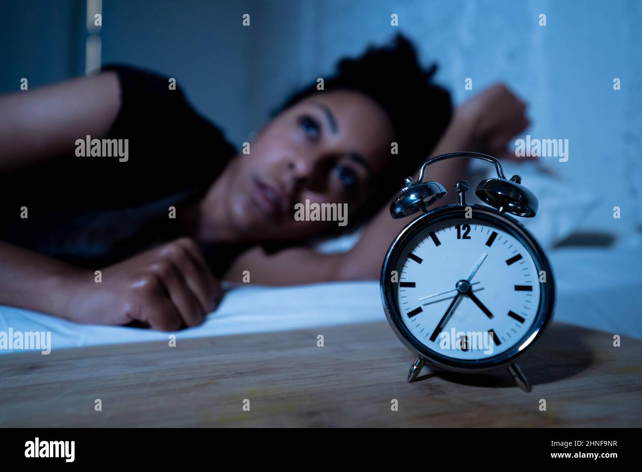 Sleepless and desperate beautiful afro american woman awake at night not able to sleep looking at clock suffering from insomnia in sleep disorder and Stock Photo
