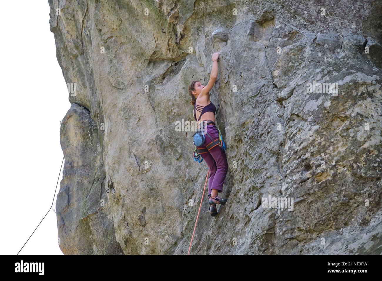 Strong female climber climbing steep wall of rocky mountain. Sportswoman difficult