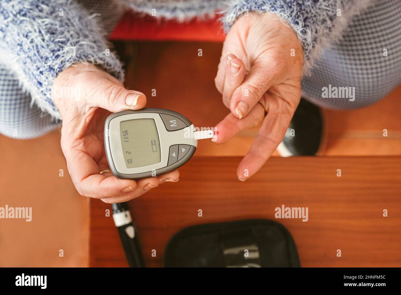 an elderly woman with a drop of blood on her finger is about to place it on the blood glucose meter. Stock Photo