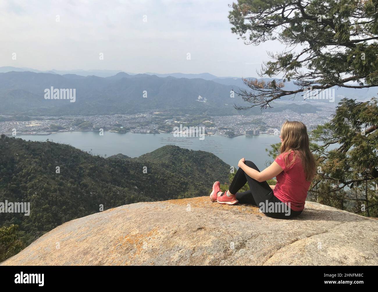 Young woman sitting on a stone, looking into the distance, Komagabayashi Peak, Miyajima, Hiroshima, Japan Stock Photo