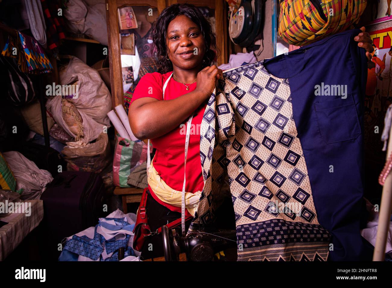 A happy African seamstress shows off the dress she has just finished sewing. Typical African suit for men just made Stock Photo