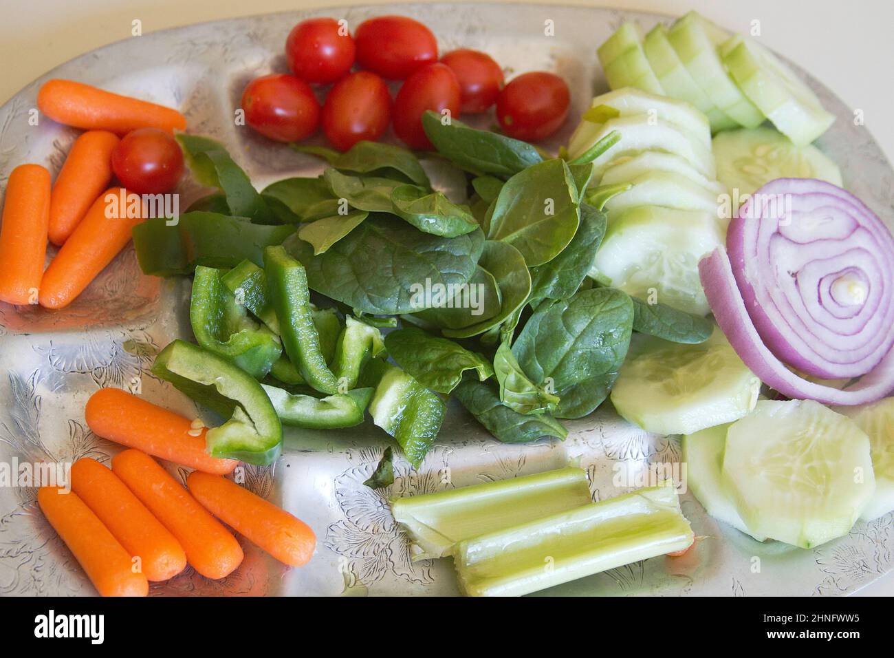 A silver platter offering colorful, snack-sized, raw organic spinach, cucumbers, plum tomatoes, red onion, baby carrots, celery and green bell peppers Stock Photo