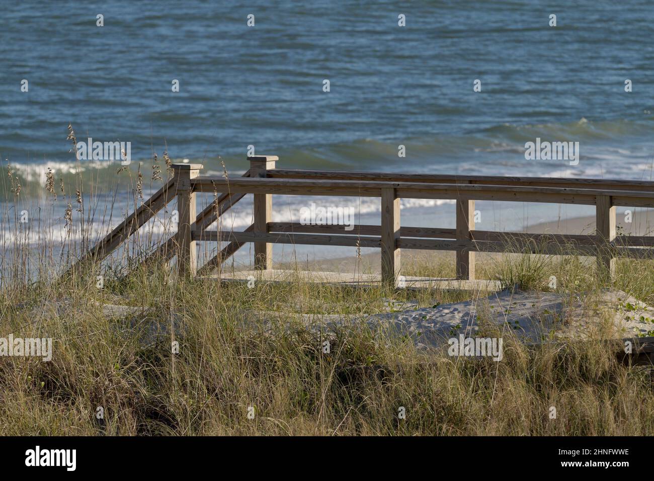 Wooden boardwalk stairway leads down to a sandy beach and the restless blue sea Stock Photo