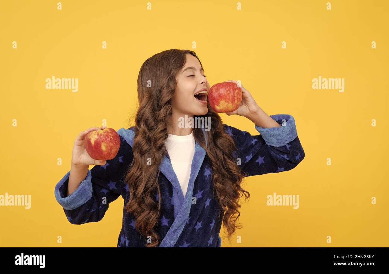 happy kid girl in sleepwear biting fresh apple fruit, organic food Stock Photo