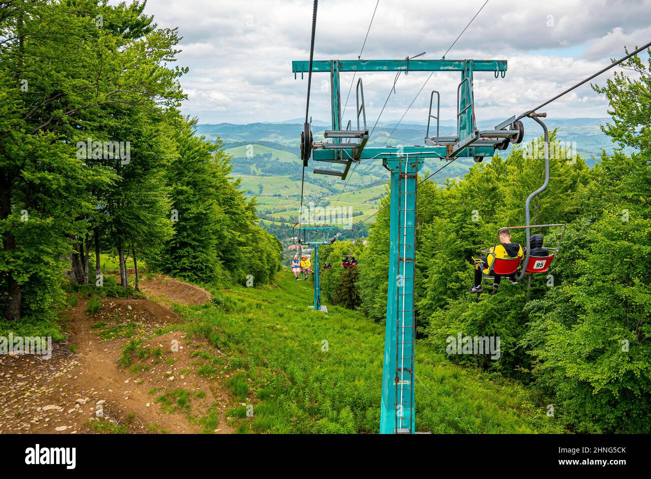 People using chair lifts through green forest against beautiful