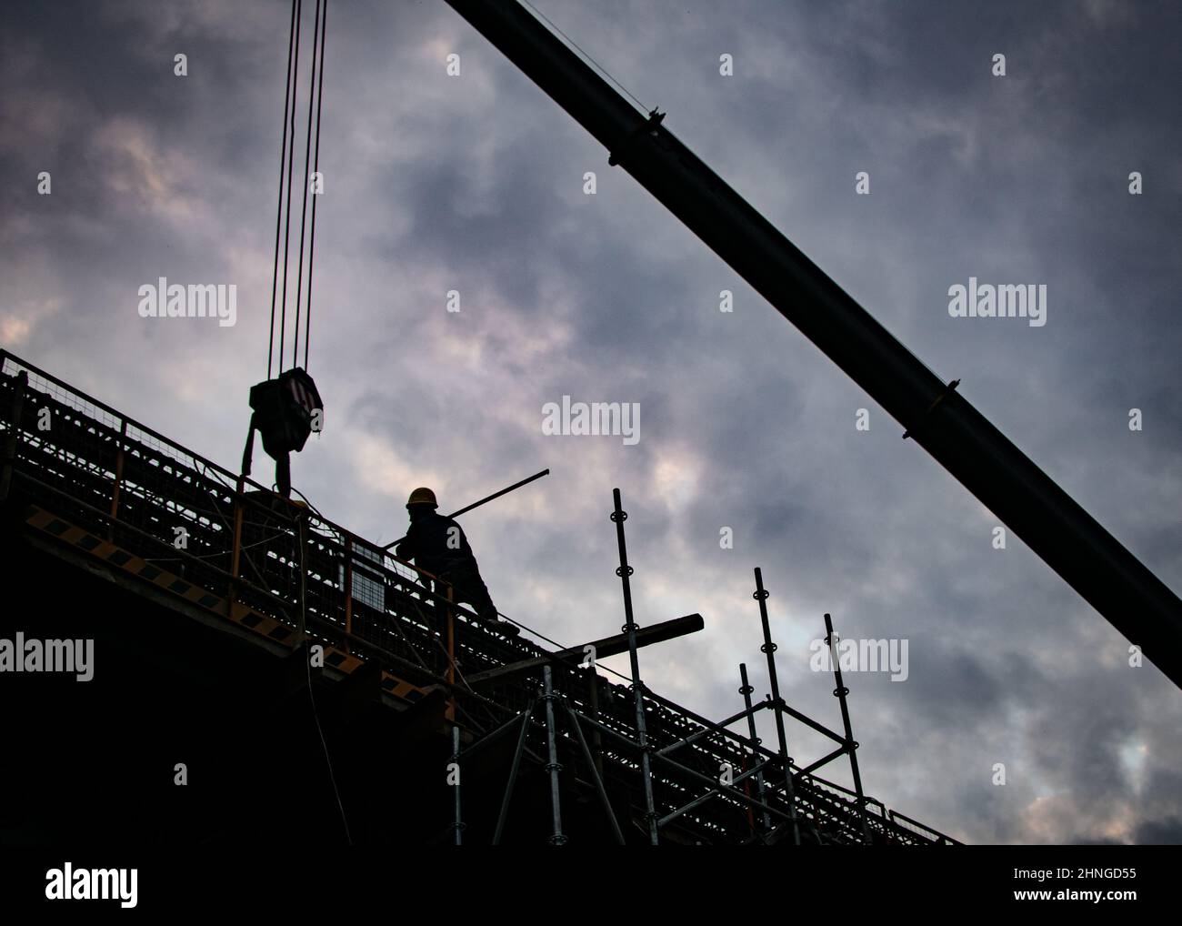 Silhouette of a worker and a crane on a construction site on cloudy sky ...
