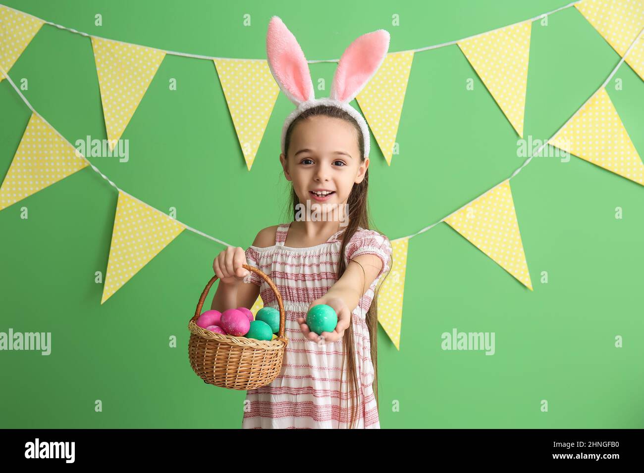Little girl with bunny ears holding basket of Easter eggs on green ...