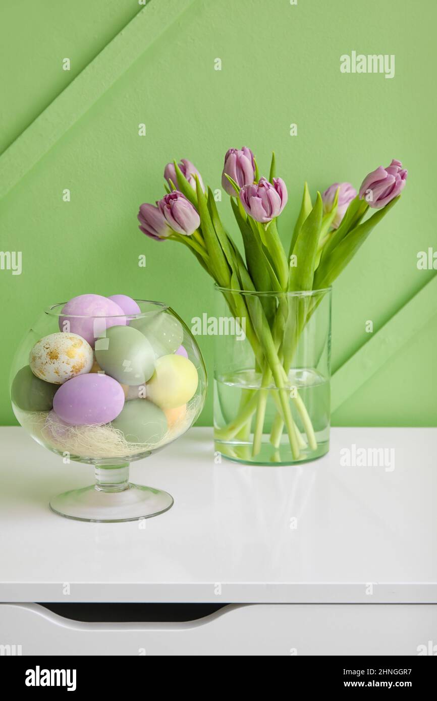 Different Easter eggs and vase with tulips on chest of drawers near ...