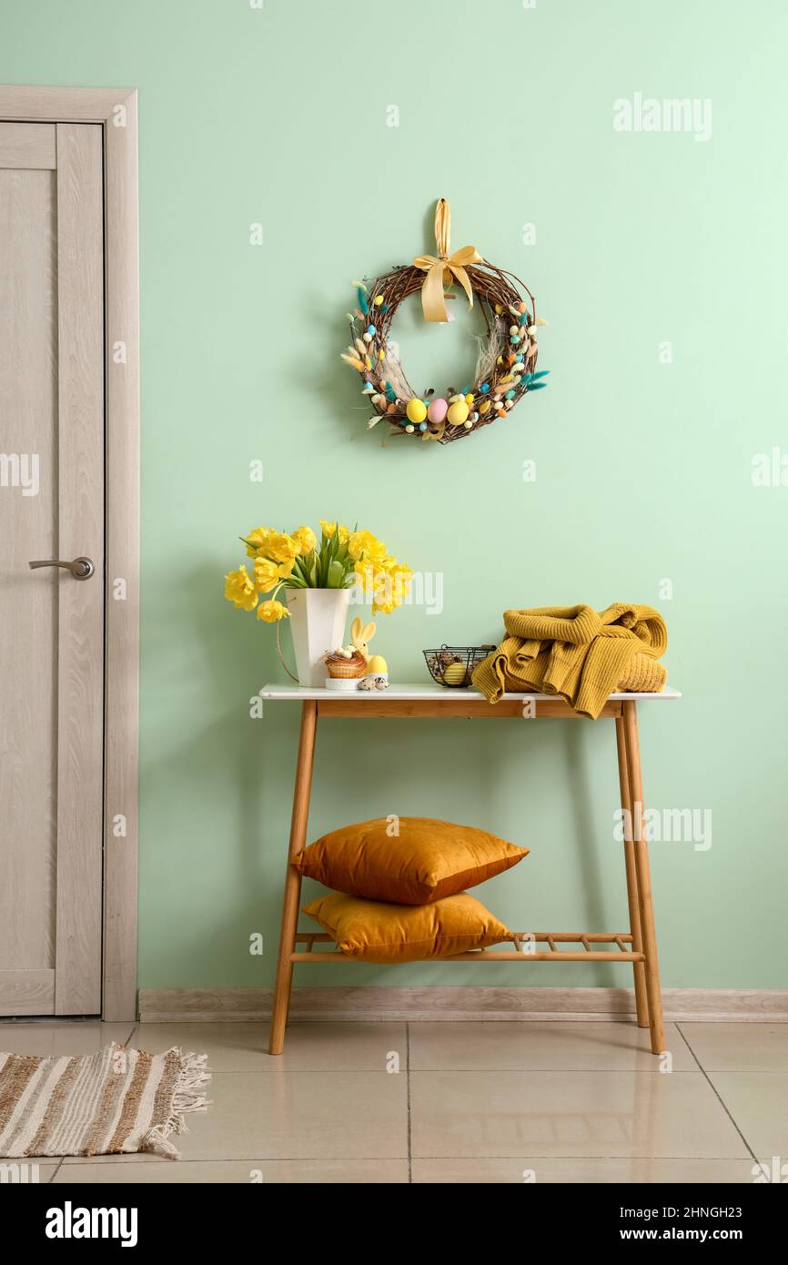 Table with beautiful tulips, knitted sweaters and stylish Easter decor near color wall in room Stock Photo