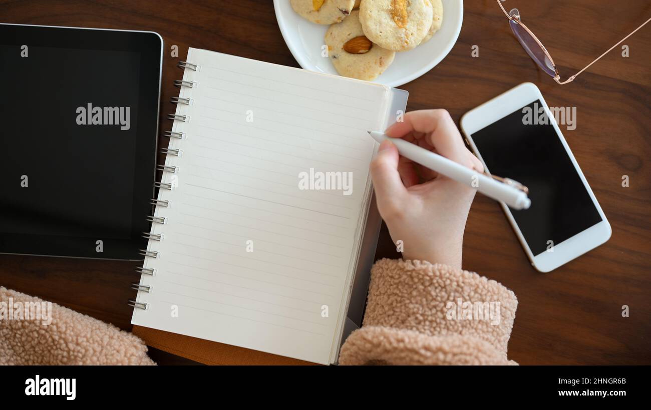 A freelance blogger sketching or drawing some picture on her notebook at cafe. A young female university student writing something on school notebook. Stock Photo