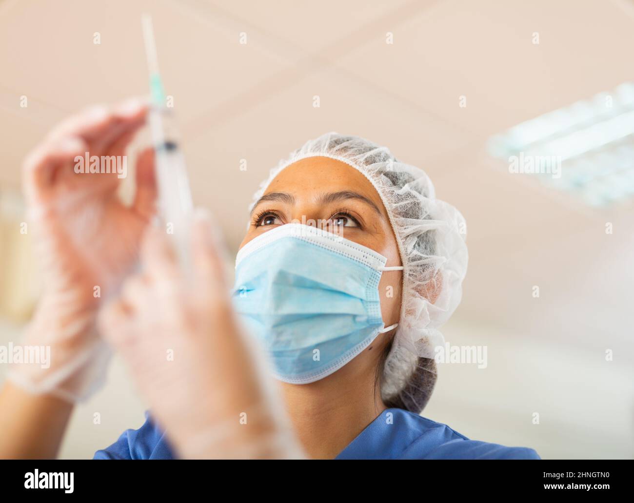 Female nurse wearing in face mask and medical uniform holding vial and syringe Stock Photo