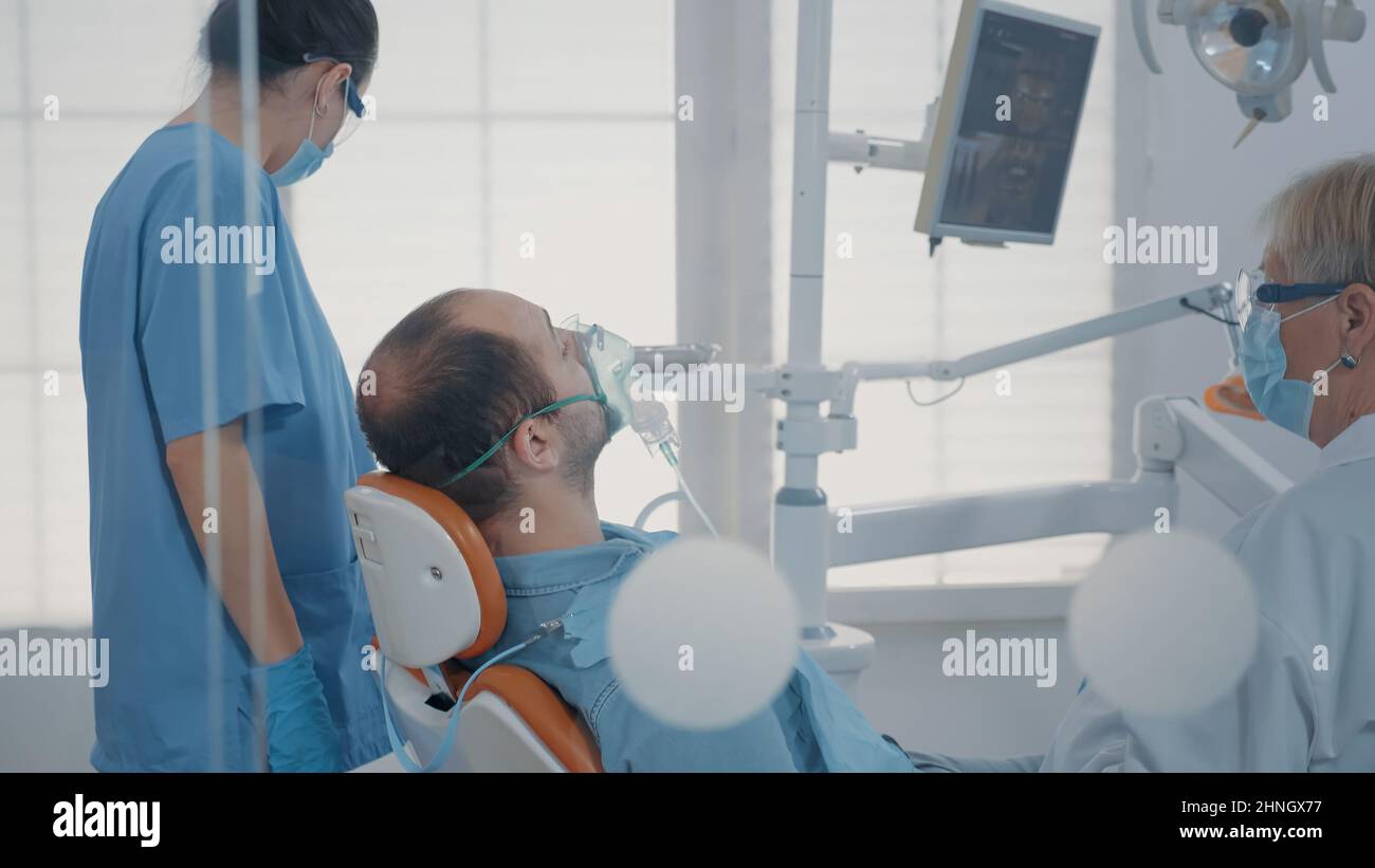 Dental assistant using oxygen mask to do anesthesia on patient before ...