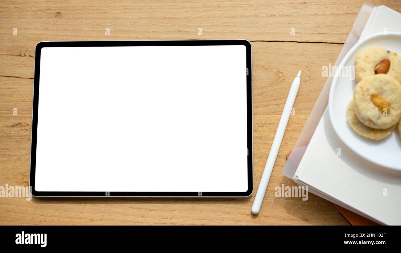 Overhead shot, A digital tablet touchpad white screen mockup, stylus pen and a plate of cookies on wooden table. Stock Photo
