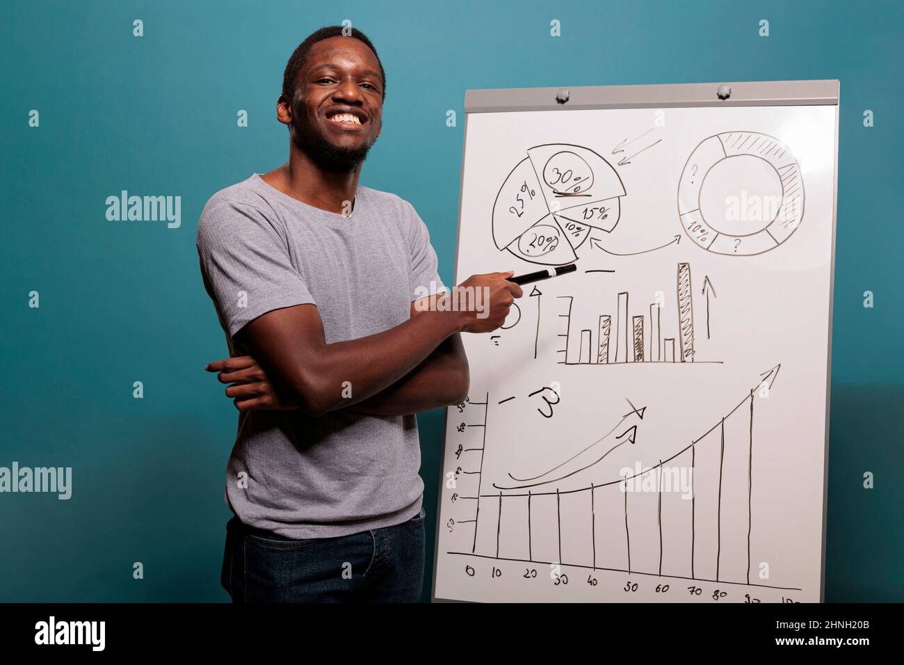 Cheerful consultant doing financial presentation on whiteboard, using charts and statistics to explain economy report in studio. Confident person using placard to plan marketing growth. Stock Photo