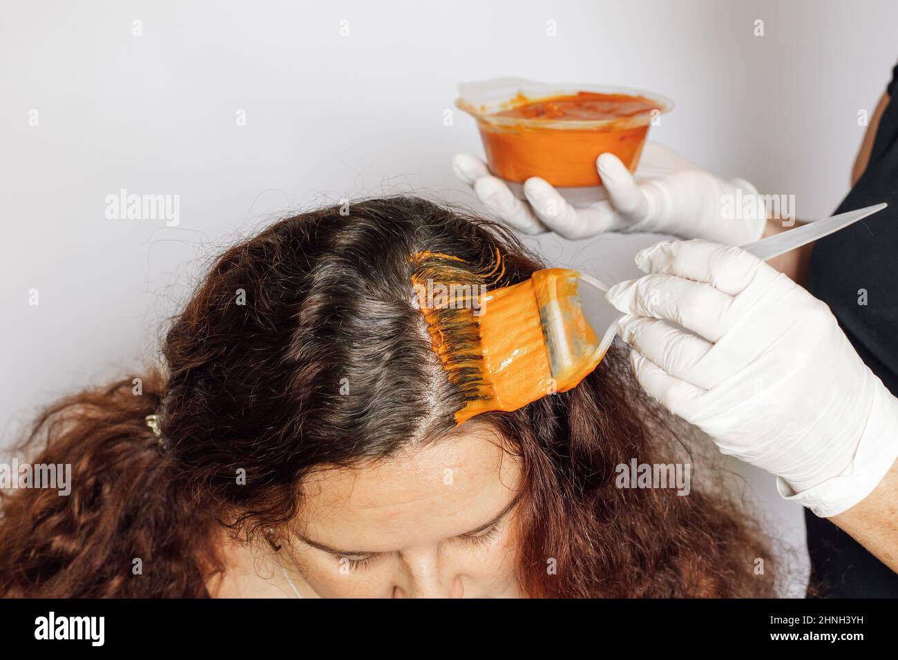 https://c8.alamy.com/comp/2HNH3YH/woman-with-coloring-brush-in-one-hand-and-hair-dye-bowl-in-the-other-applying-red-substance-on-woman-hair-roots-hair-coloring-at-home-getting-rid-of-2HNH3YH.jpg