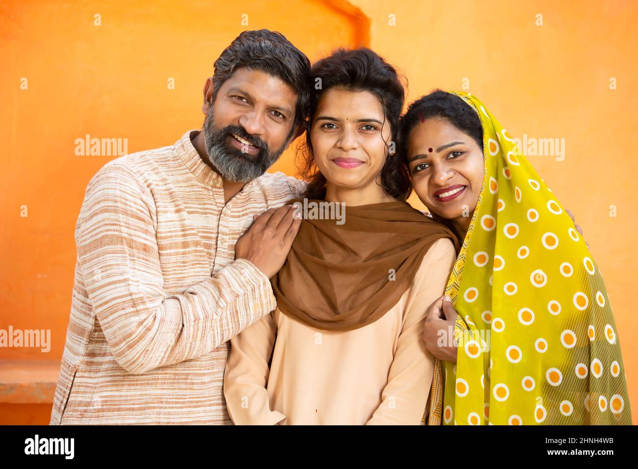 Portrait of happy rural Indian family, young girl in school uniform with her parents, Beard man and woman in sari standing with daughter. looking at c Stock Photo