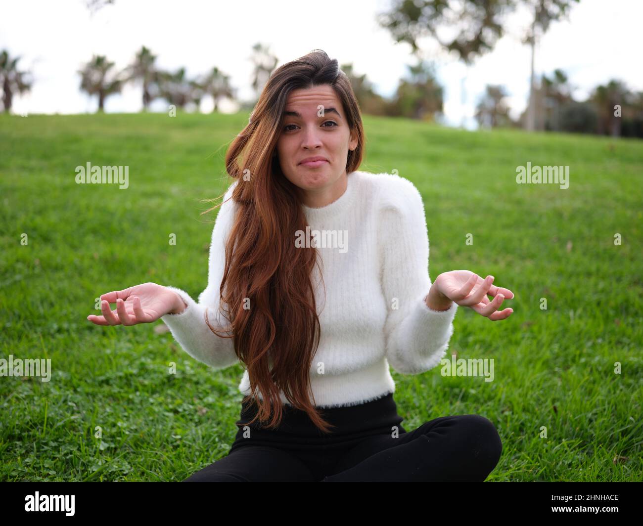 Young adult woman with a doubt shrugging shoulders in the park Stock Photo