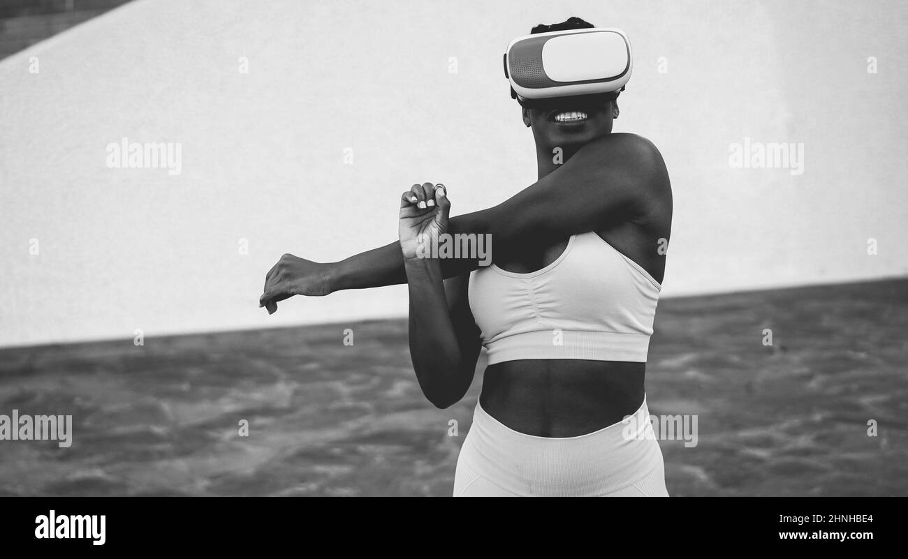 Fit african woman wearing virtual reality headset during sport workout routine - Metaverse concept - Focus on vr goggles - Black and white editing Stock Photo