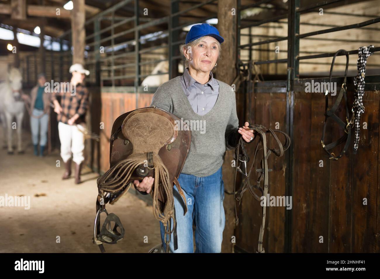 Female rancher carrying horse tack and saddle in horse farm Stock Photo