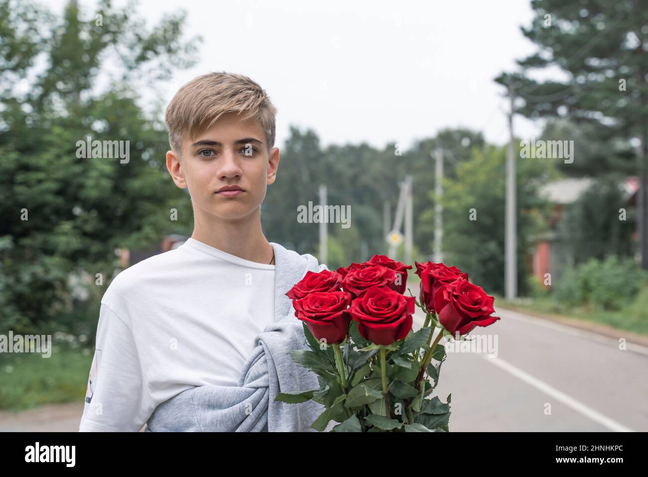 Handsome teenager holds a bouquet of red roses in his hands.  Stock Photo