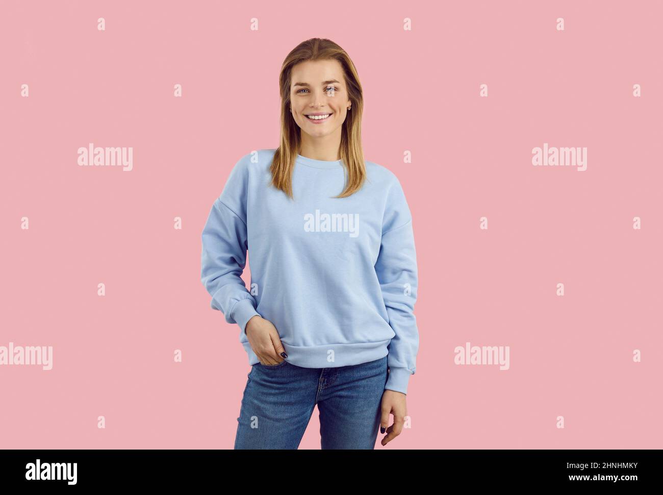 Happy smiling young girl in sweatshirt and jeans posing isolated on pink background Stock Photo