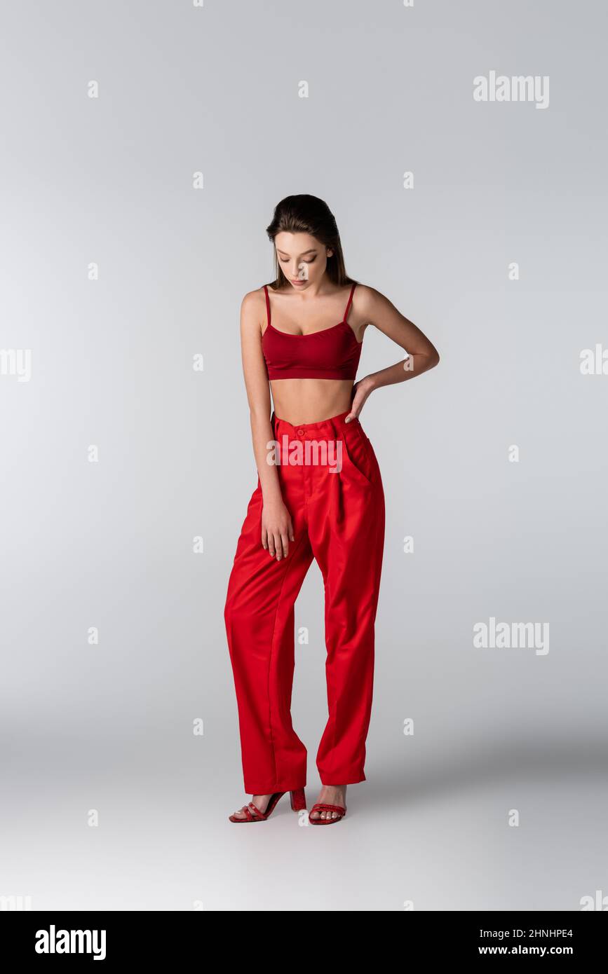 full length of pretty model in red outfit posing with hand on hip on grey Stock Photo
