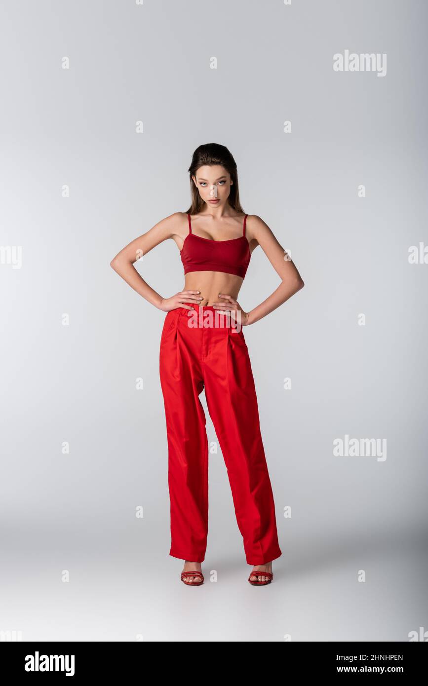 full length of pretty model in red outfit posing with hands on hips on grey Stock Photo