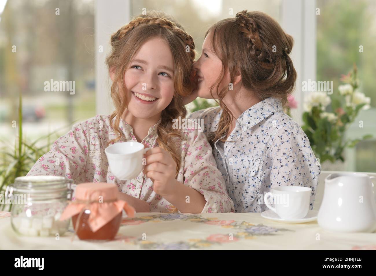 Two smiling little girls drinking tea at home sharing secret Stock Photo