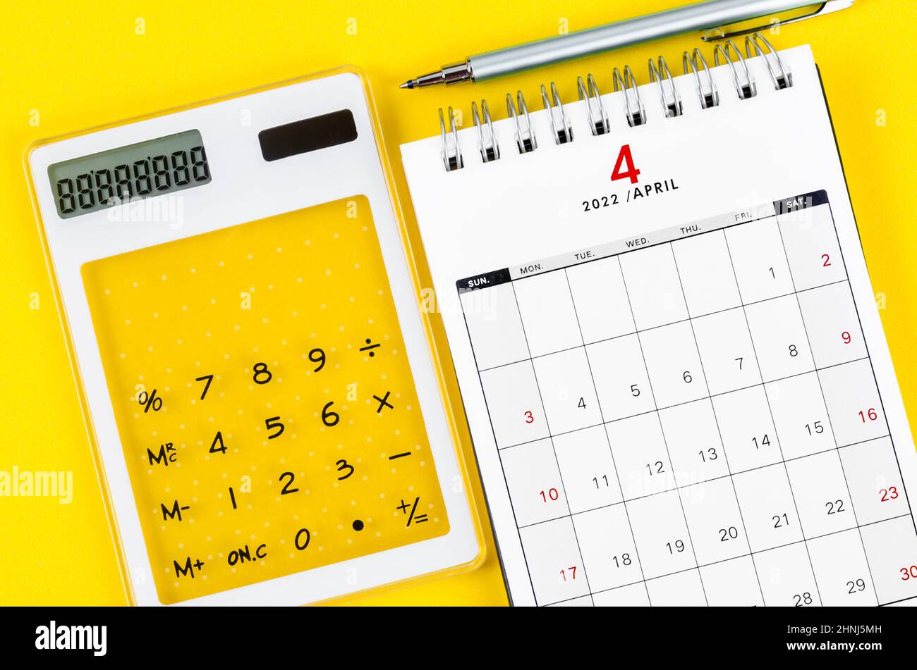 The April 2022 desk calendar with calculator and pen on yellow background. Stock Photo