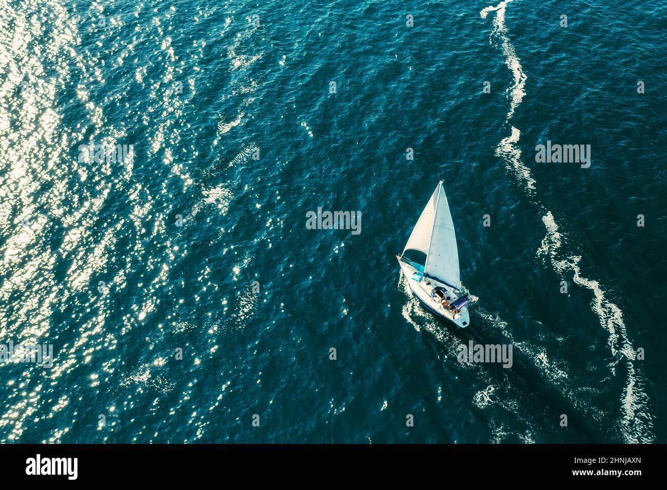 ROVINJ, CZECH REPUBLIC - JULY 03 2021: Sailing vessel leaves white foam trace on surface of Adriatic sea. Bright sunlight reflecting from surface of calm sea rippling water. Aerial view Stock Photo