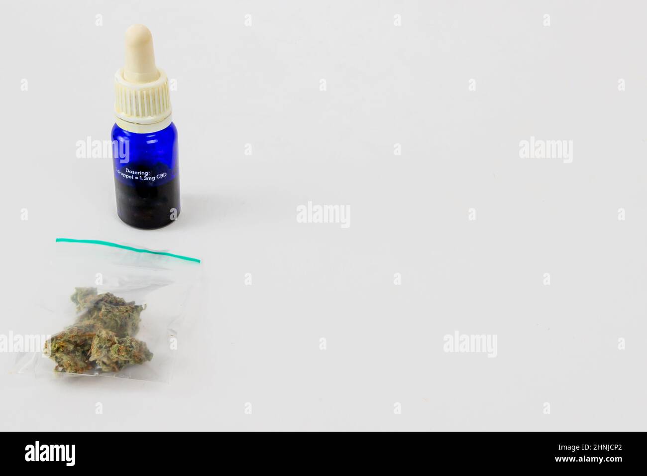One gram of dried medical marijuana buds in a clear plastic bag, blue glass bottle with 10 ml of CBD oil on a white studio background of cannabis extr Stock Photo