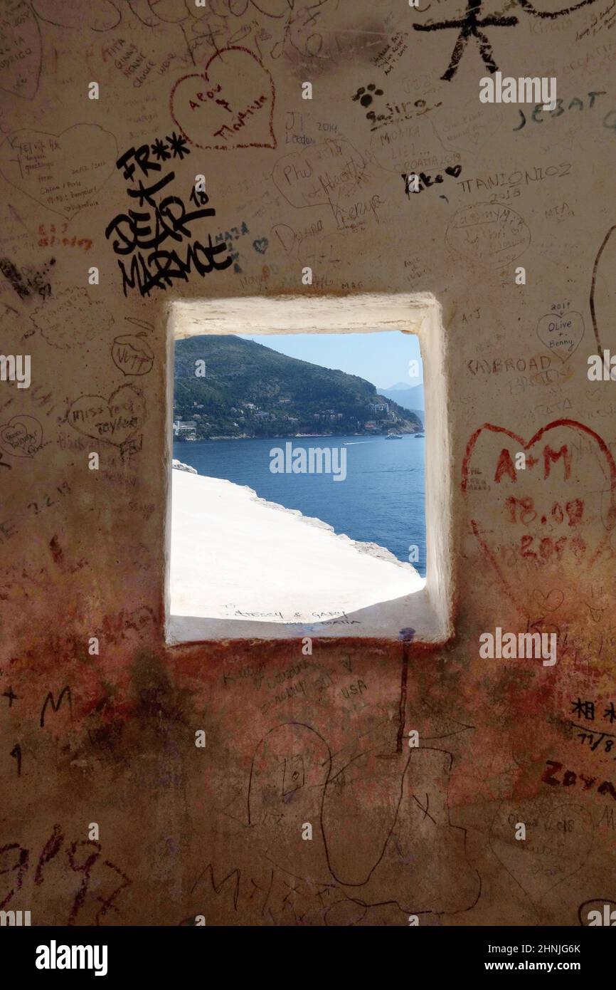 Graffiti on the inside of a gun turret on the old town walls in Dubrovnik with the Adriatic Sea beyond. Stock Photo