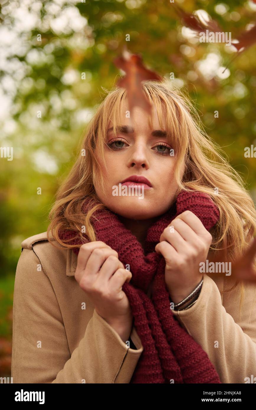 Portrait of young blonde woman wearing a scarf with autumn background and leaves Stock Photo