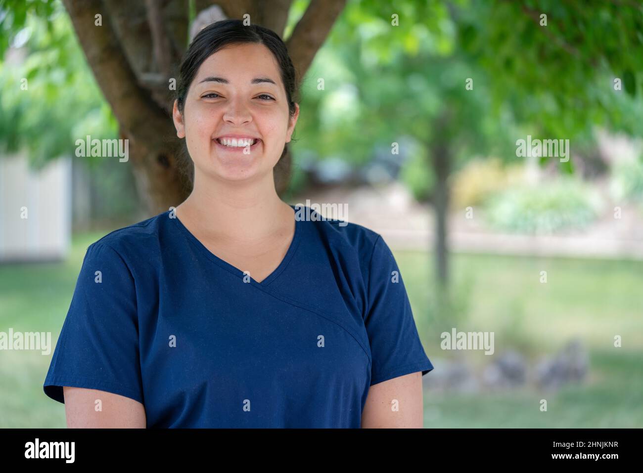 Beautiful, female, essential, front line home worker smiling. Long-term personal health care worker wearing navy blue medical scrubs in Canada. Stock Photo