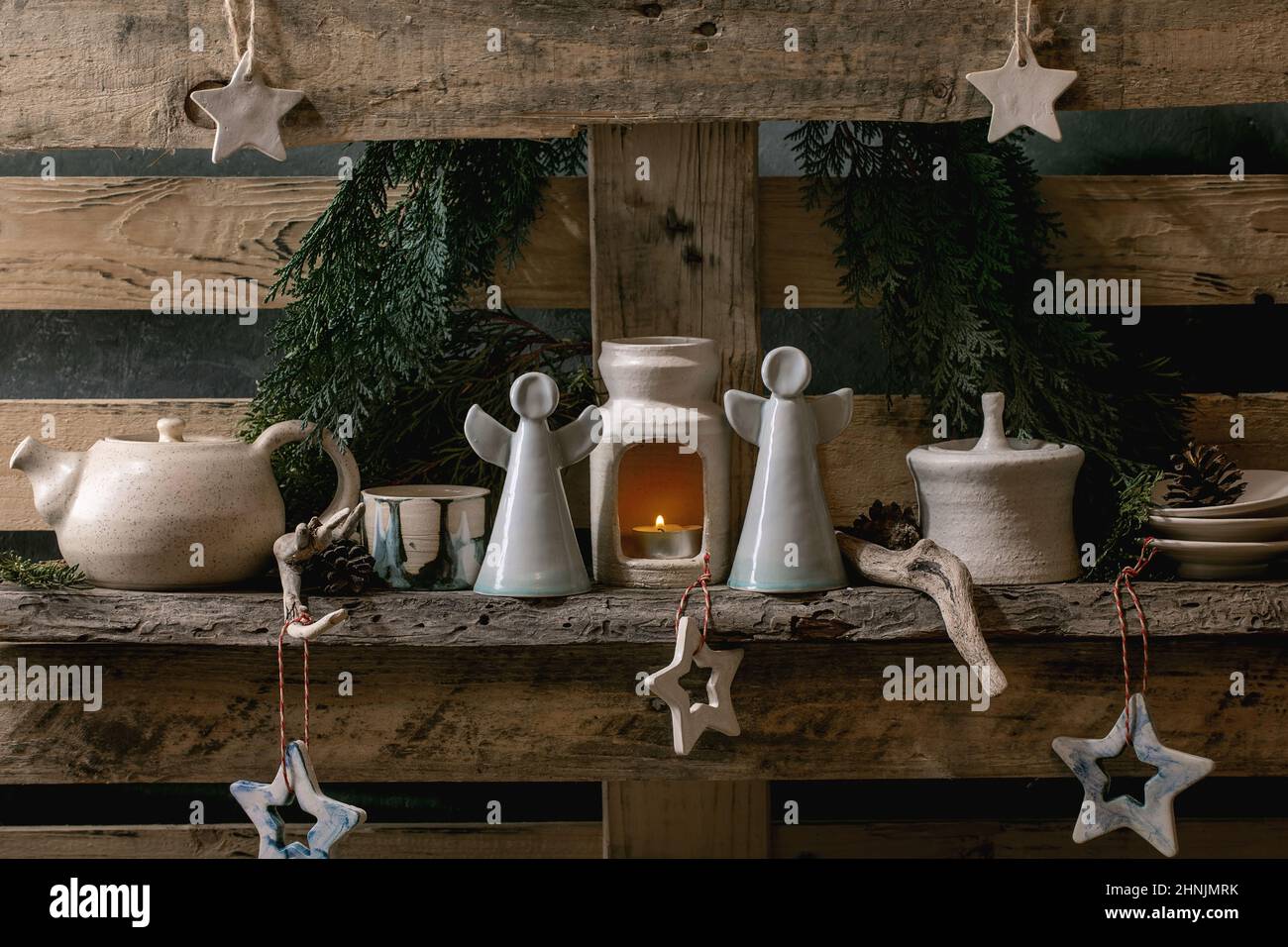 Christmas fashion rustic style interior decor with craft wood, ceramics and angels on old wooden pallet shelf and thuja branches at background. Scandi Stock Photo