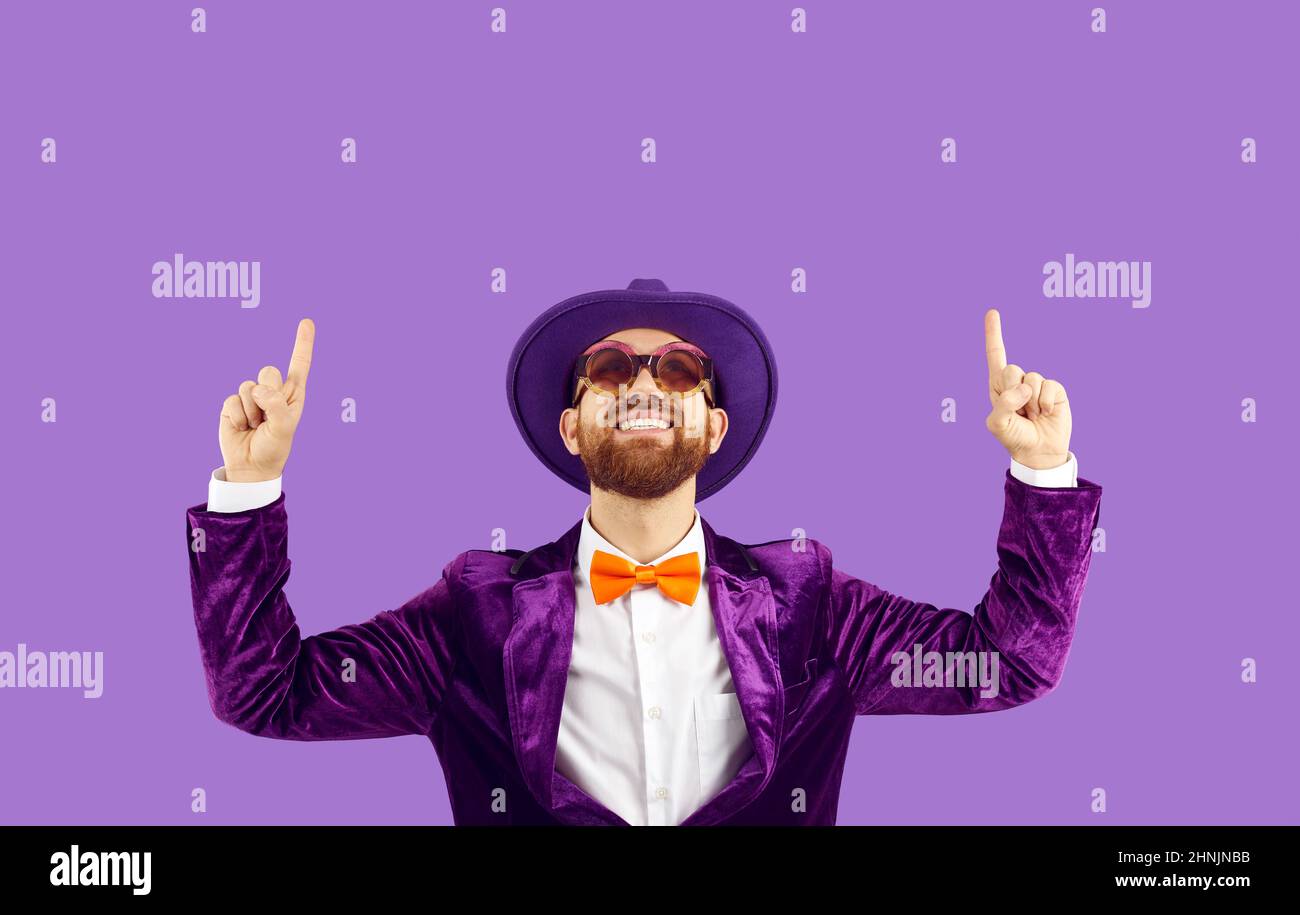 Cool cheerful man in funny glamorous outfit shows up on copy space on purple background. Stock Photo