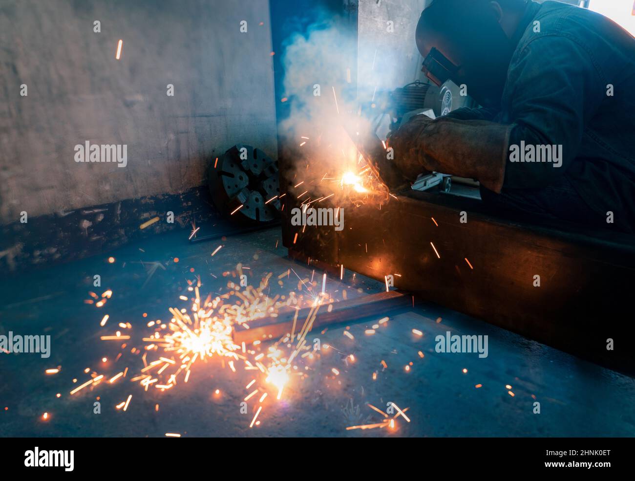 Welder welding metal with argon arc welding machine and has welding sparks. Man wears a welding mask and gloves. Safety in industrial workplace. Welder working with safety. Steel industry technology. Stock Photo