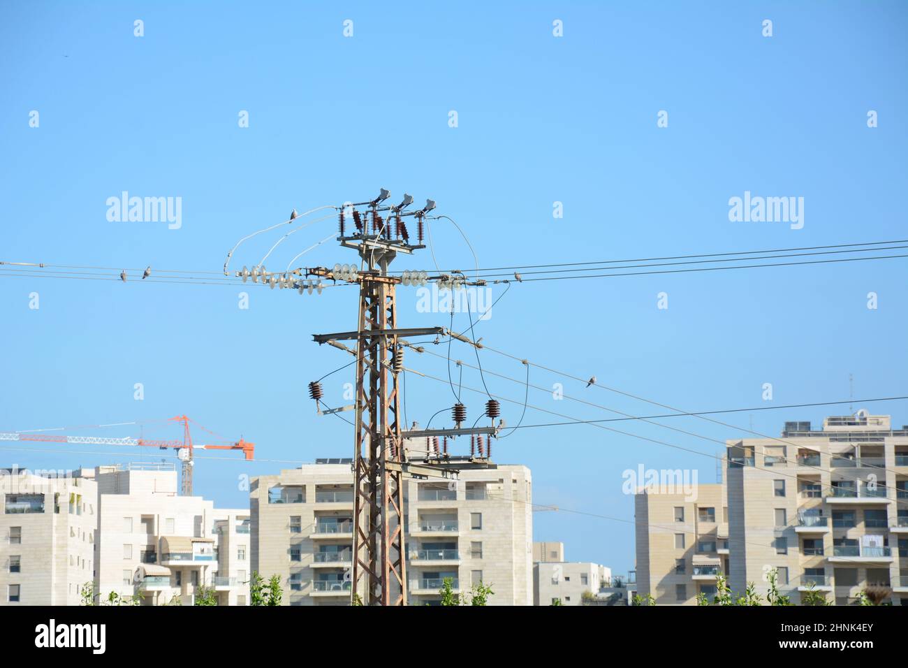 Low angle close-up view of the top part of an electricity distribution pylon and power lines under blue sky Stock Photo