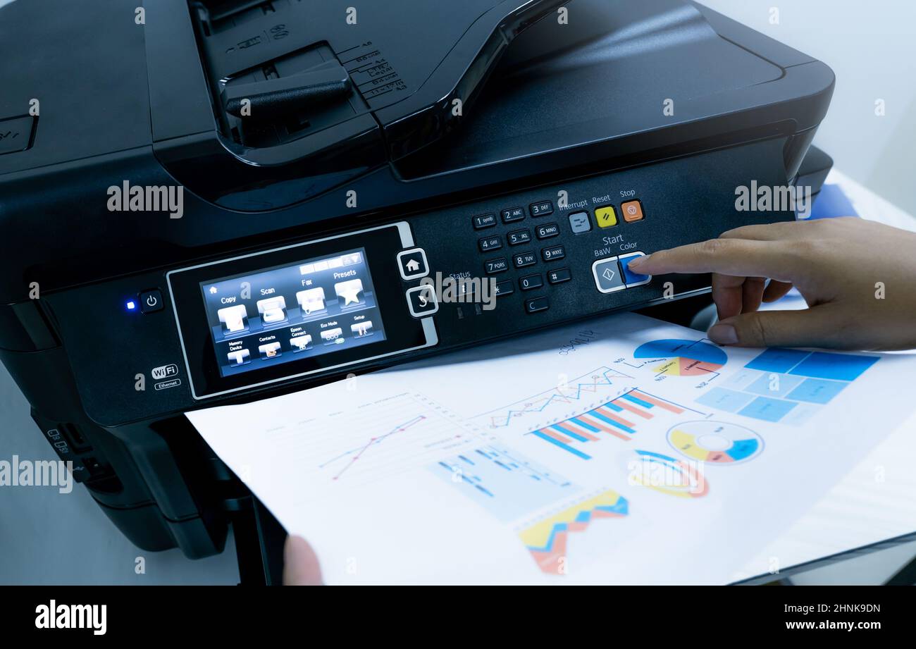 Office worker prints paper on multifunction laser printer. Copy, print, scan, and fax machine in office. Document and paper work. Print technology. Ha Stock Photo