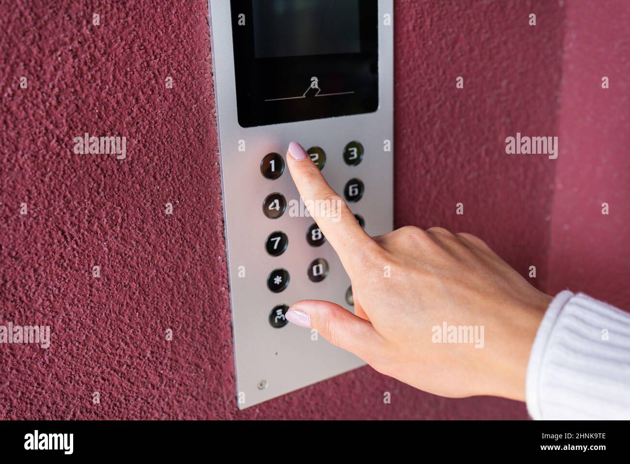 A young woman dials the apartment code on the panel of an electronic Protection and