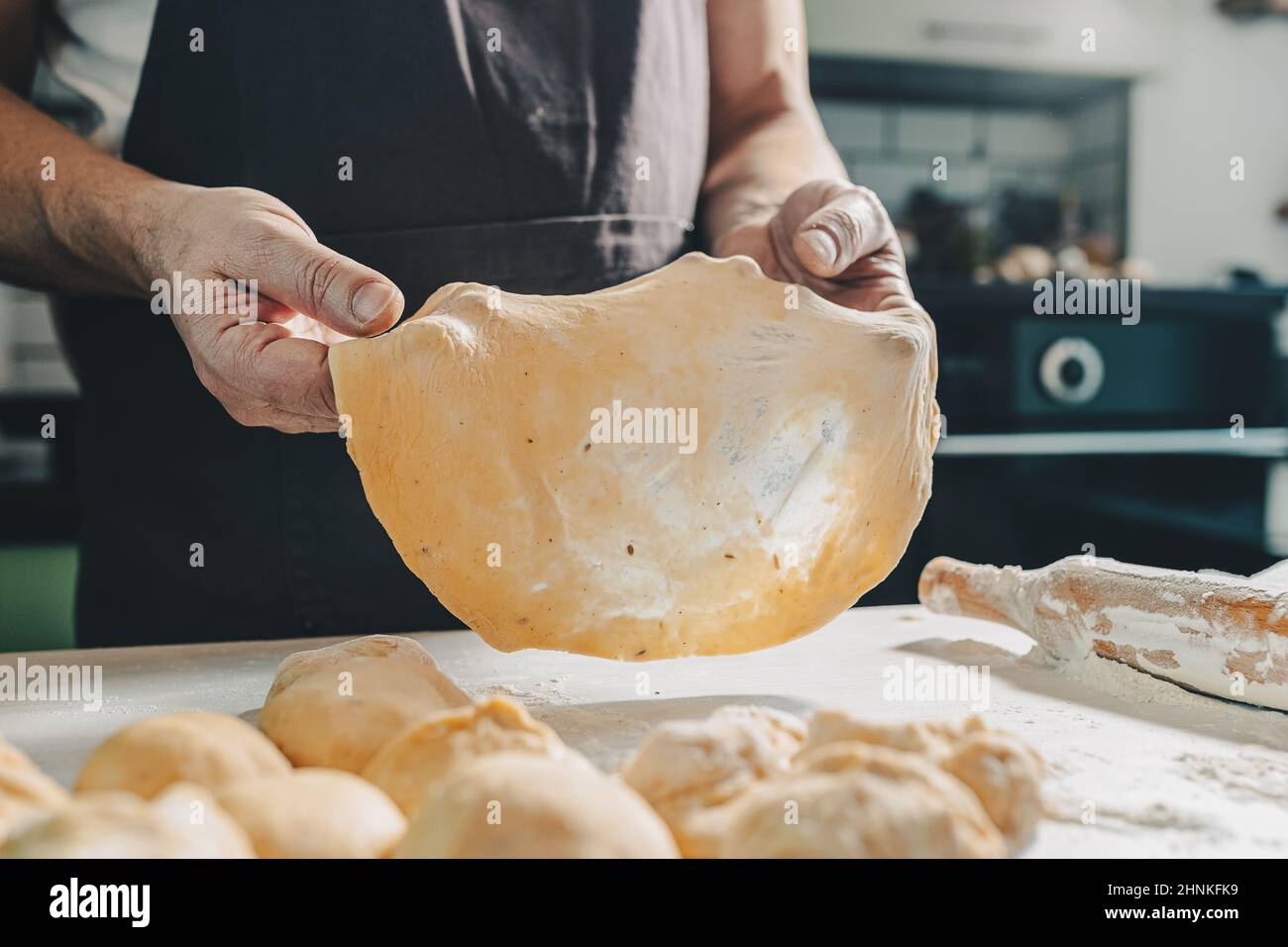 muscular hands of male baker hold thinly rolled dough. Cooking in home kitchen dough for pizza or pita bread. man prepares homemade cakes Stock Photo