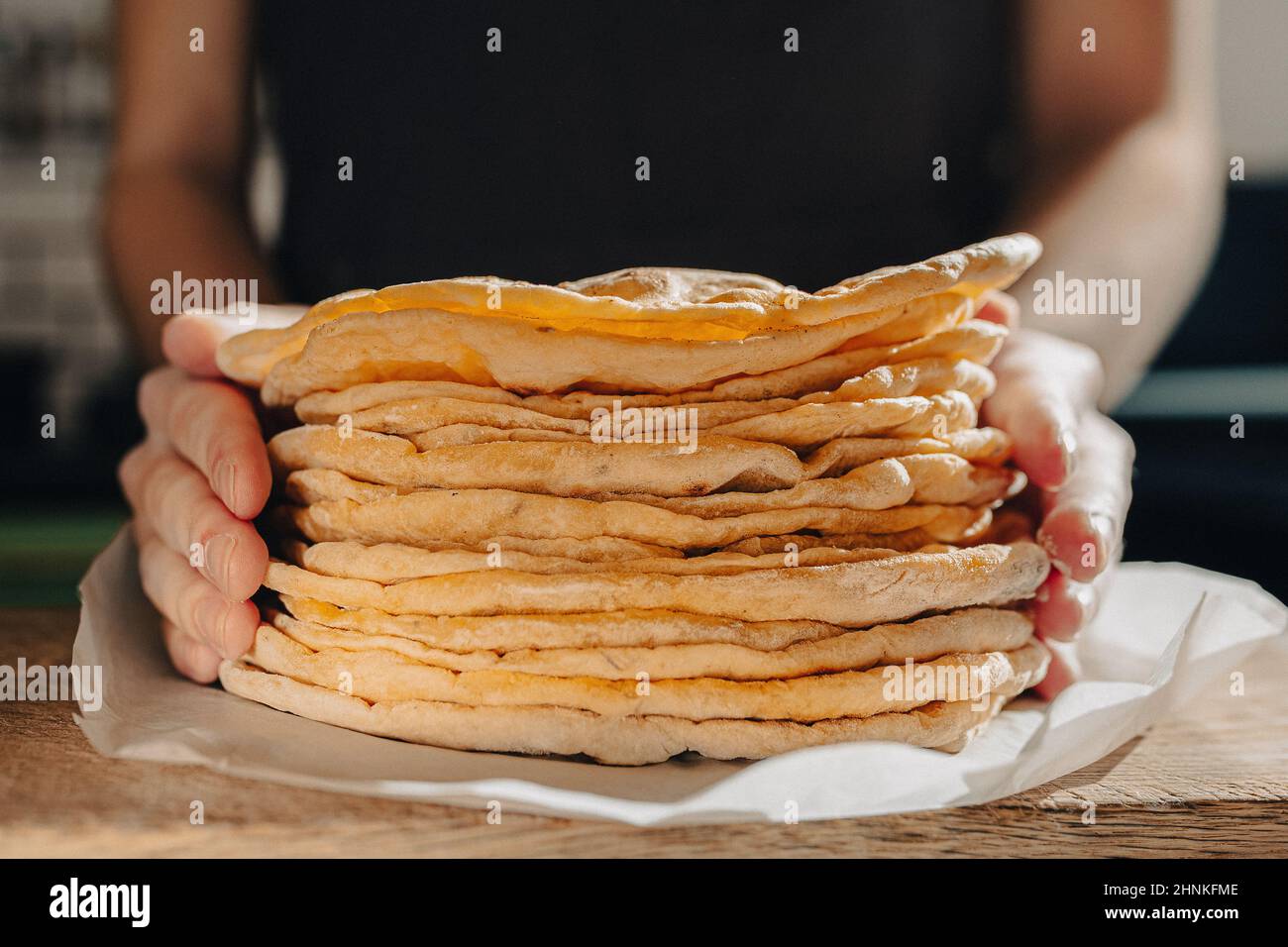 Thin round cakes of lavash are stacked, hands of cook stretch lavash forward for testing. Spanish flatbread or armenian lavash close-up Stock Photo