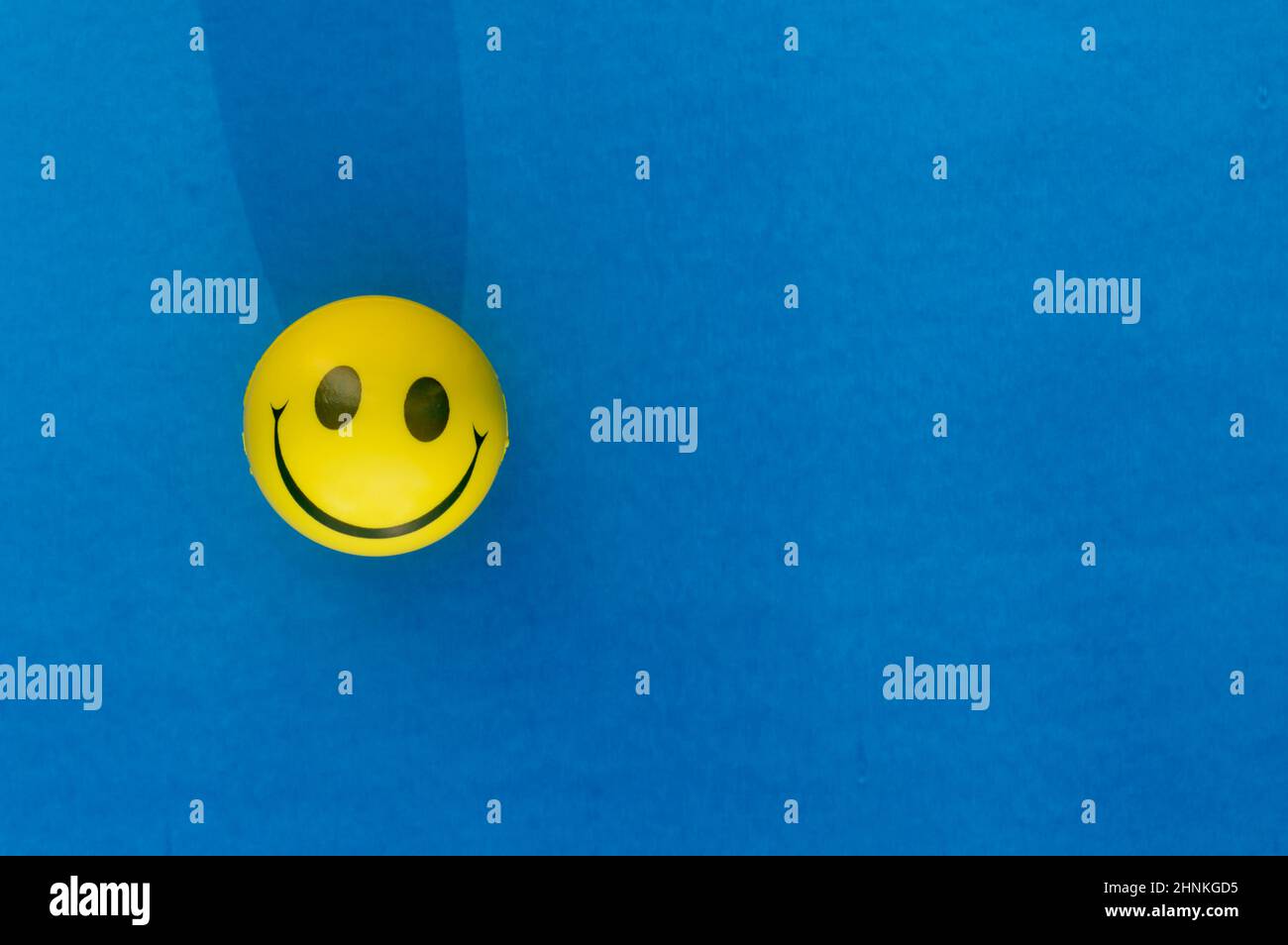 Anthropomorphic smiley face expression of a Squeeze Ball or Stress Ball isolated on blue background. Table top view. Close up. Happy smile background Stock Photo
