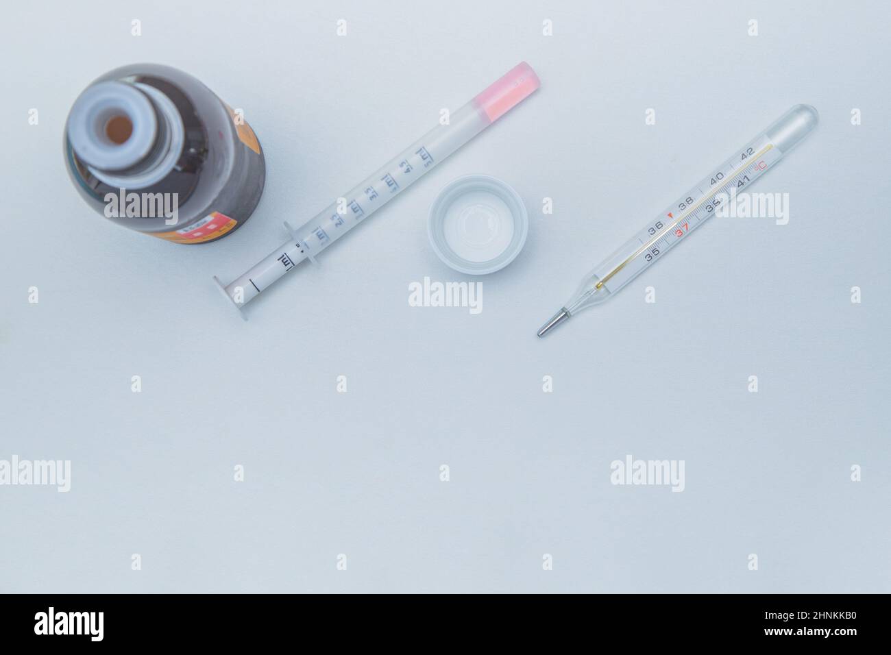 A medicine with a measuring syringe and a thermometer lies a white background. Stock Photo